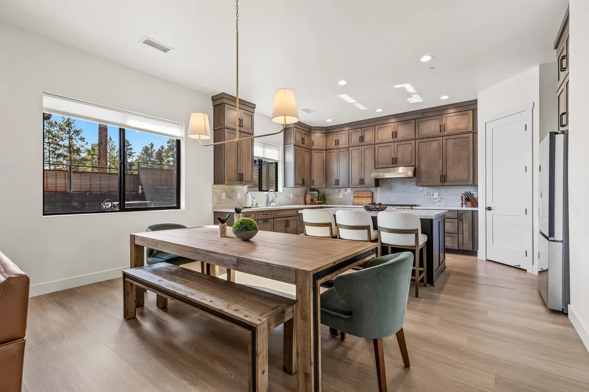 A large wooden dining table sits at the center, surrounded by modern kitchen cabinetry with natural light streaming in from a window. The setting is warm and welcoming, suggesting group meals or celebrations that might follow campus events or evenings out downtown.