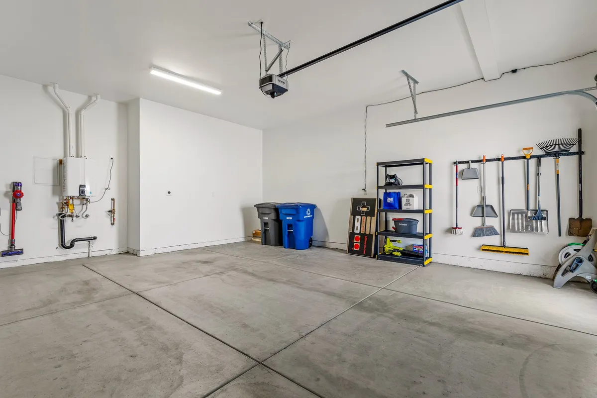 An interior shot of a clean, well-organized garage featuring shelves with tools, garbage bins, and a spotless concrete floor. The space feels practical and ready for storing vehicles and outdoor equipment.