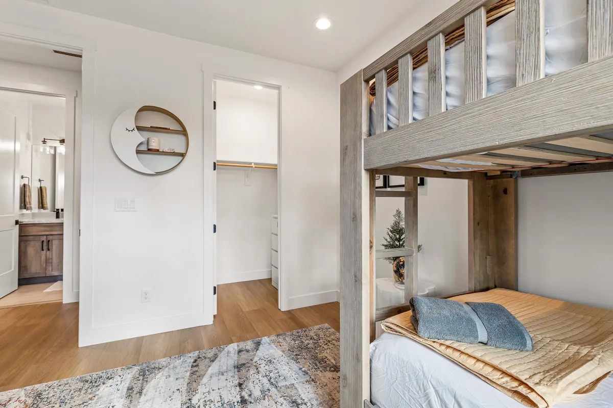 A playful and comfortable kids' bunk room with a sturdy bunk bed, decorative pillows, a round mirror, and wooden floors. The space feels fun and inviting, perfect for sleepovers or quiet play.