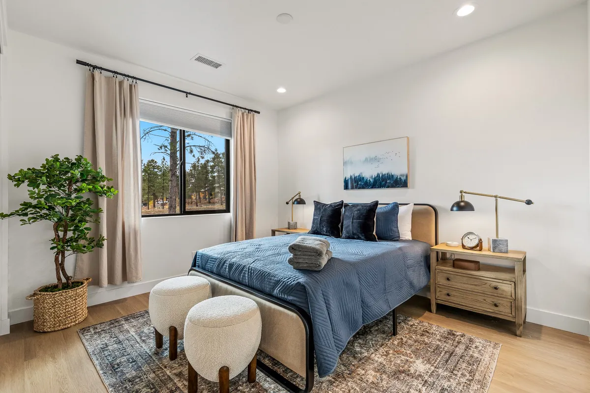 A bright bedroom with a comfortable bed, large window offering a scenic view, a leafy green plant, and a simple nightstand. The decor emphasizes a calming, private retreat perfect for unwinding at any time of day.