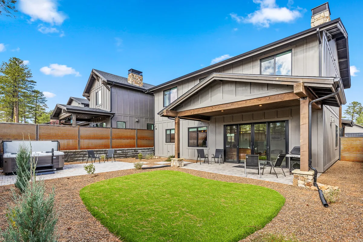 The backyard is shown with a well-manicured lawn, patio seating beneath a wooden pergola, a visible hot tub, and a stone pathway. The layout is open and inviting, ideal for group gatherings or peaceful solitude. Subtle evening lighting and the arrangement of outdoor furniture evoke both lively and contemplative moods.