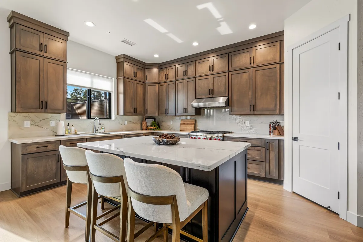 A bright, modern kitchen featuring a large island, wooden cabinetry, stainless steel appliances, and an abundance of natural light streaming through the windows. The open layout offers plenty of space for group meal prep or casual dining.