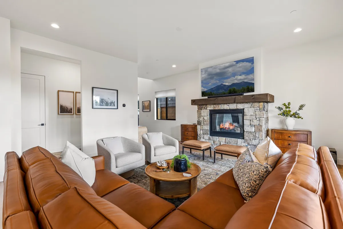 An inviting living room centered around a stone fireplace with a brown leather sofa and round coffee table. The decor includes a mountain view painting, creating a warm setting perfect for storytelling or game nights.