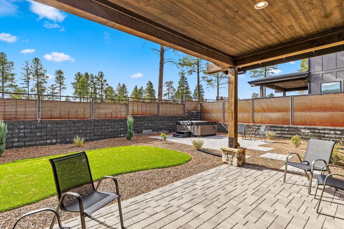 This exterior image showcases a beautifully landscaped lawn with a private hot tub, inviting patio seating, and a wooden pergola, all set against a tranquil natural backdrop. The space is clearly designed for relaxation and outdoor entertaining, with plenty of room to soak in the scenery or enjoy stargazing.