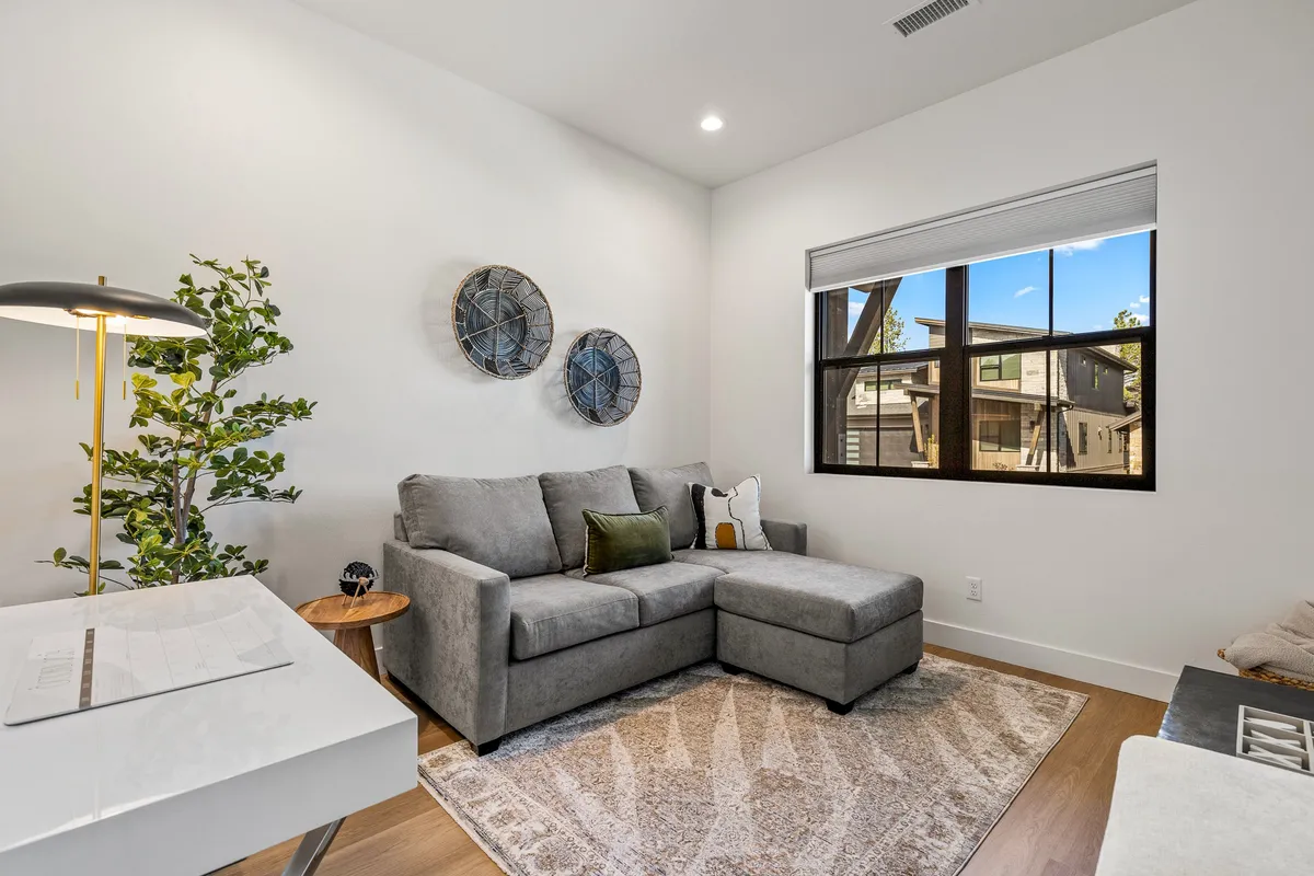 A cozy living area featuring a comfortable sofa, decorative wall art, a floor lamp, and a window view. The space is arranged for casual conversations or relaxed reading, providing a warm and inviting atmosphere for gatherings.