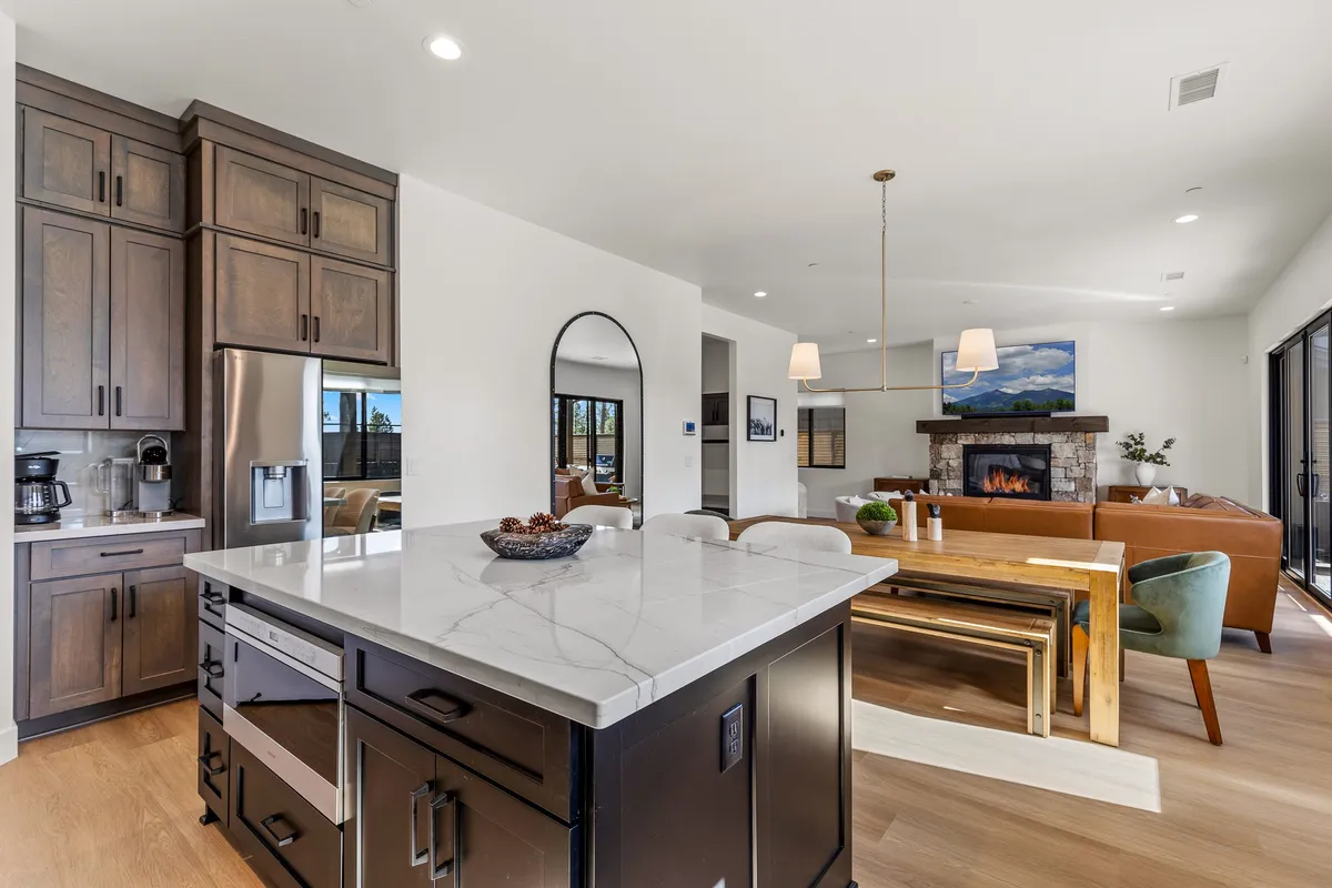 The image highlights a spacious, open-plan interior featuring a kitchen island, fireplace, dining table, sofa, and artwork. The area exudes warmth and is ideal for entertaining, dining, or relaxing after a day exploring downtown or campus events.
