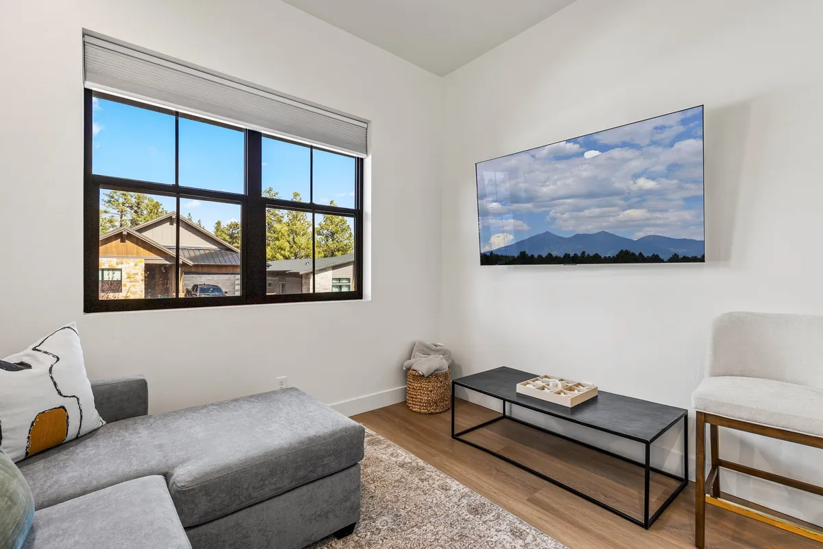 A comfortable living room featuring a large window with a view, a television displaying a mountain landscape, and a cozy sofa. The window opens up the space to the outdoors, hinting at the beautiful natural surroundings just outside.