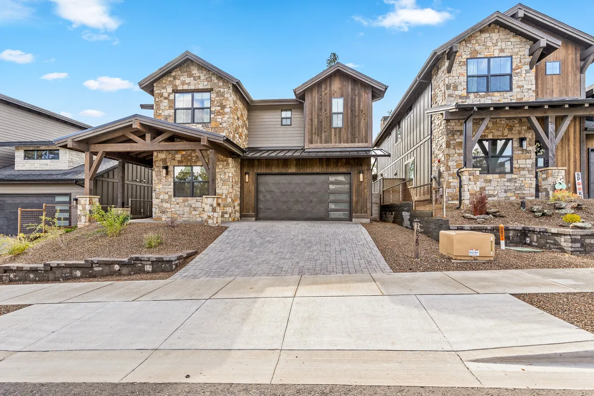 This exterior image showcases the home's stone facade with wooden beams and a modern garage door, all flanked by a landscaped front yard. The garage is prominent, making it clear that vehicle and gear storage is a key feature.