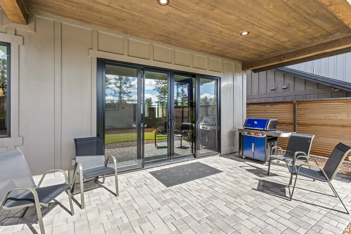 A cozy patio scene with outdoor seating, a grill, and large glass doors opening to the backyard. The area is arranged for barbecuing and relaxed outdoor dining, with comfortable furniture that invites guests to linger. The setting feels casual and perfect for family cookouts or unwinding after a day of adventure.